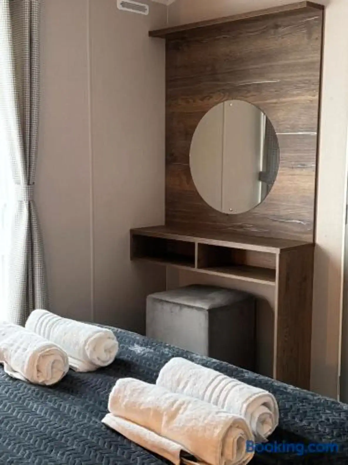 Cozy bedroom with a wooden vanity and round mirror, featuring neatly arranged towels