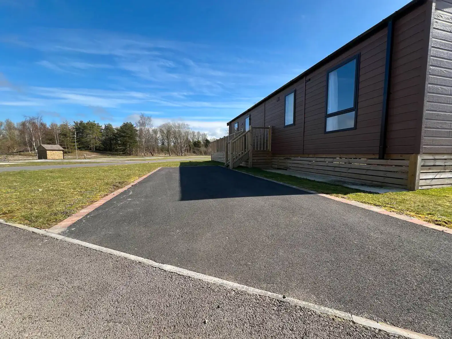 Paved driveway leading to a brown cabin with a grassy area