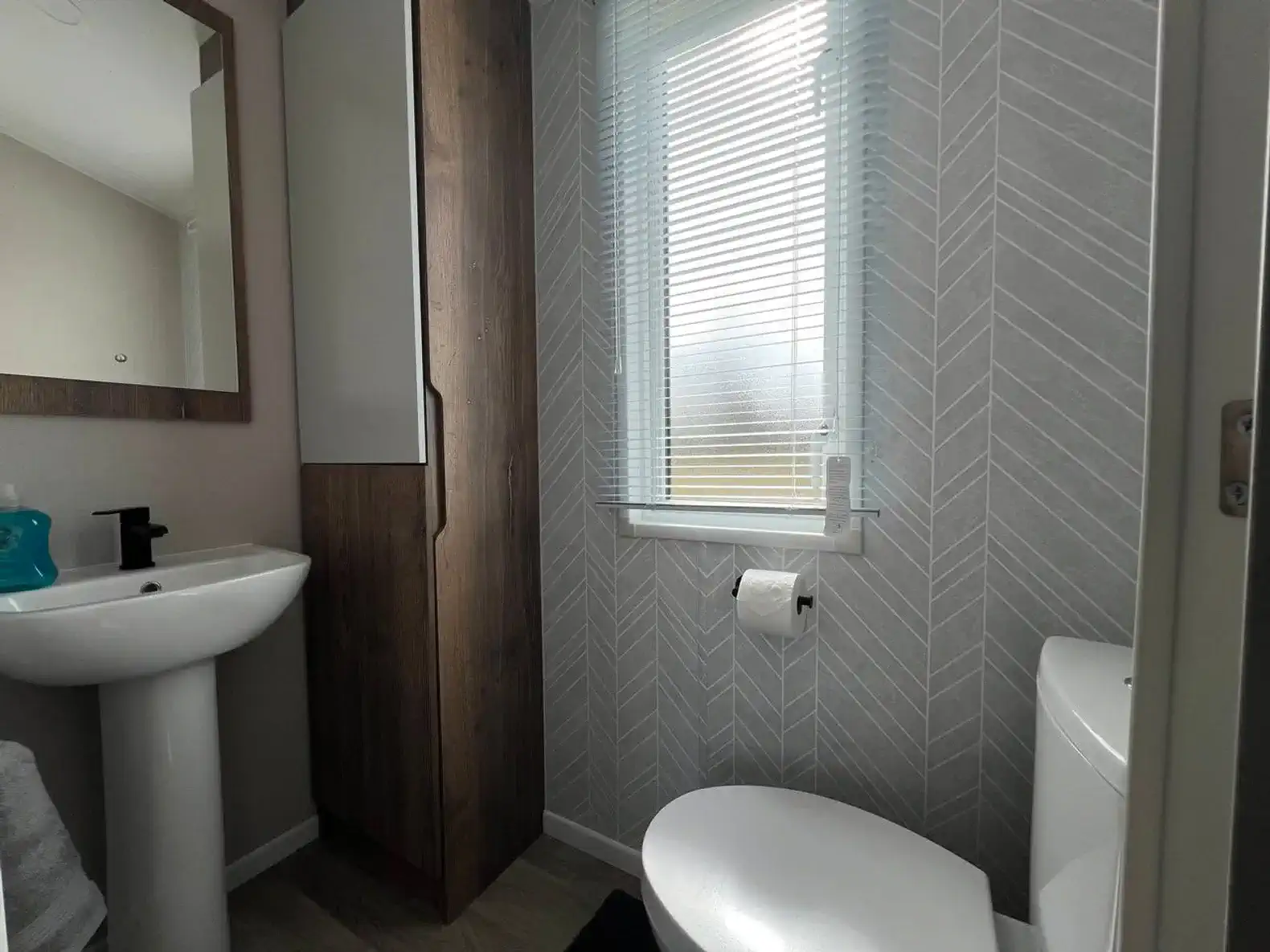 Modern bathroom featuring a sink, toilet, and window with blinds