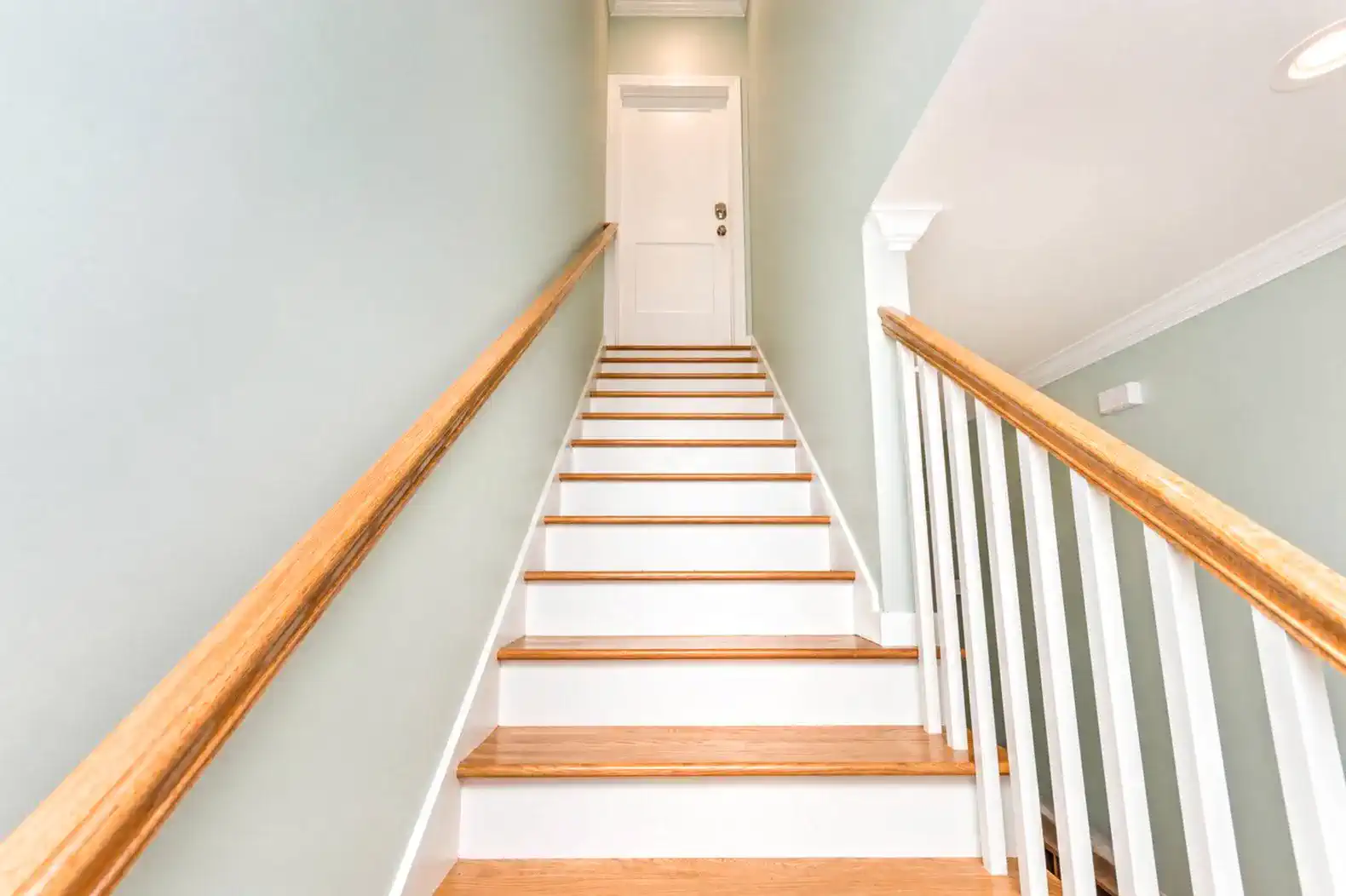 Staircase leading to a door with wooden handrails and light green walls