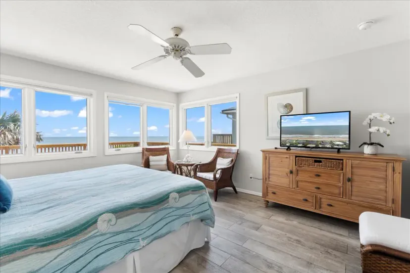 Cozy master bedroom with ocean views and a TV, featuring wicker chairs and a light color scheme