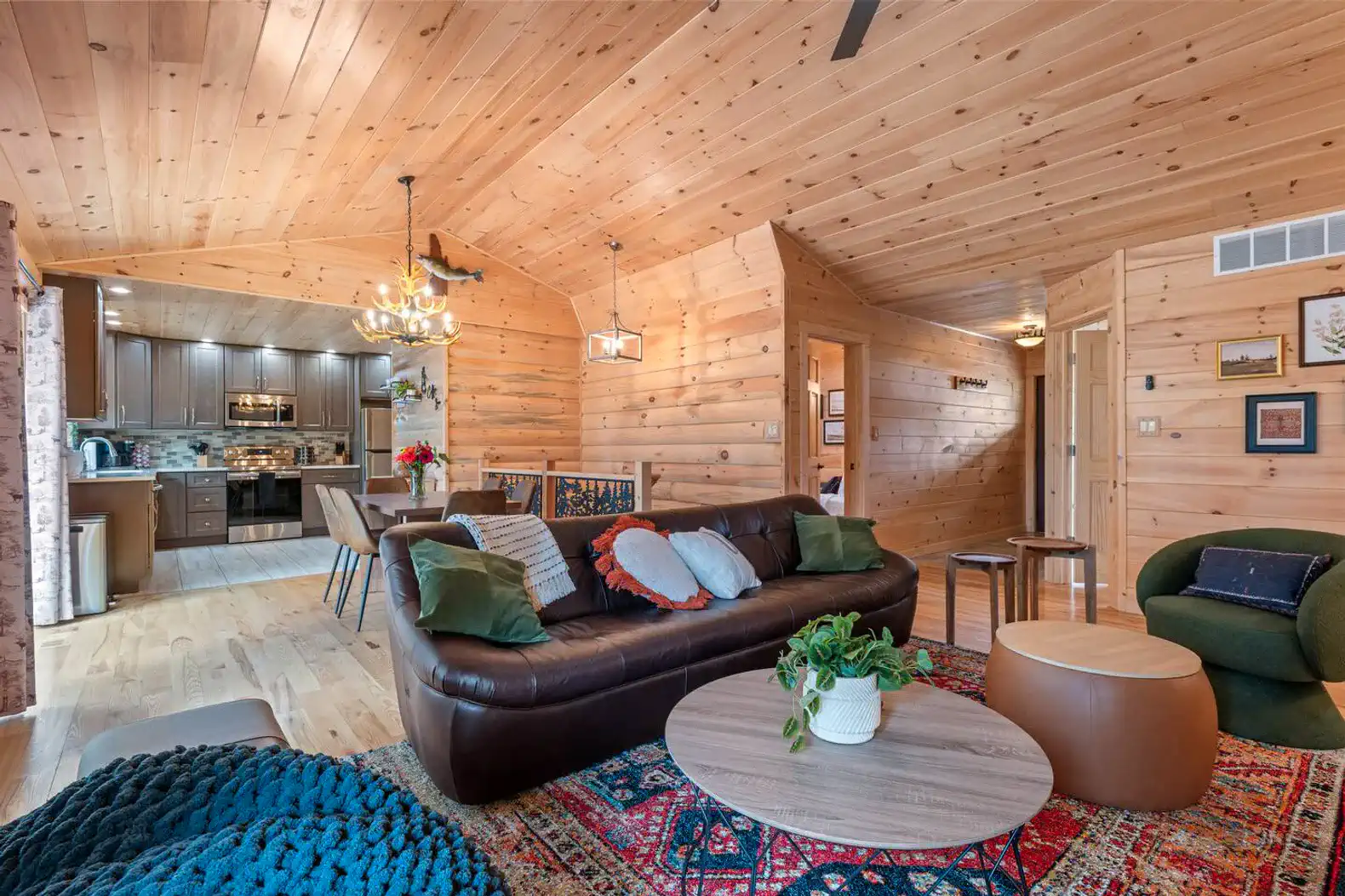 Cozy living room with wooden walls, comfortable seating, and a view into the kitchen