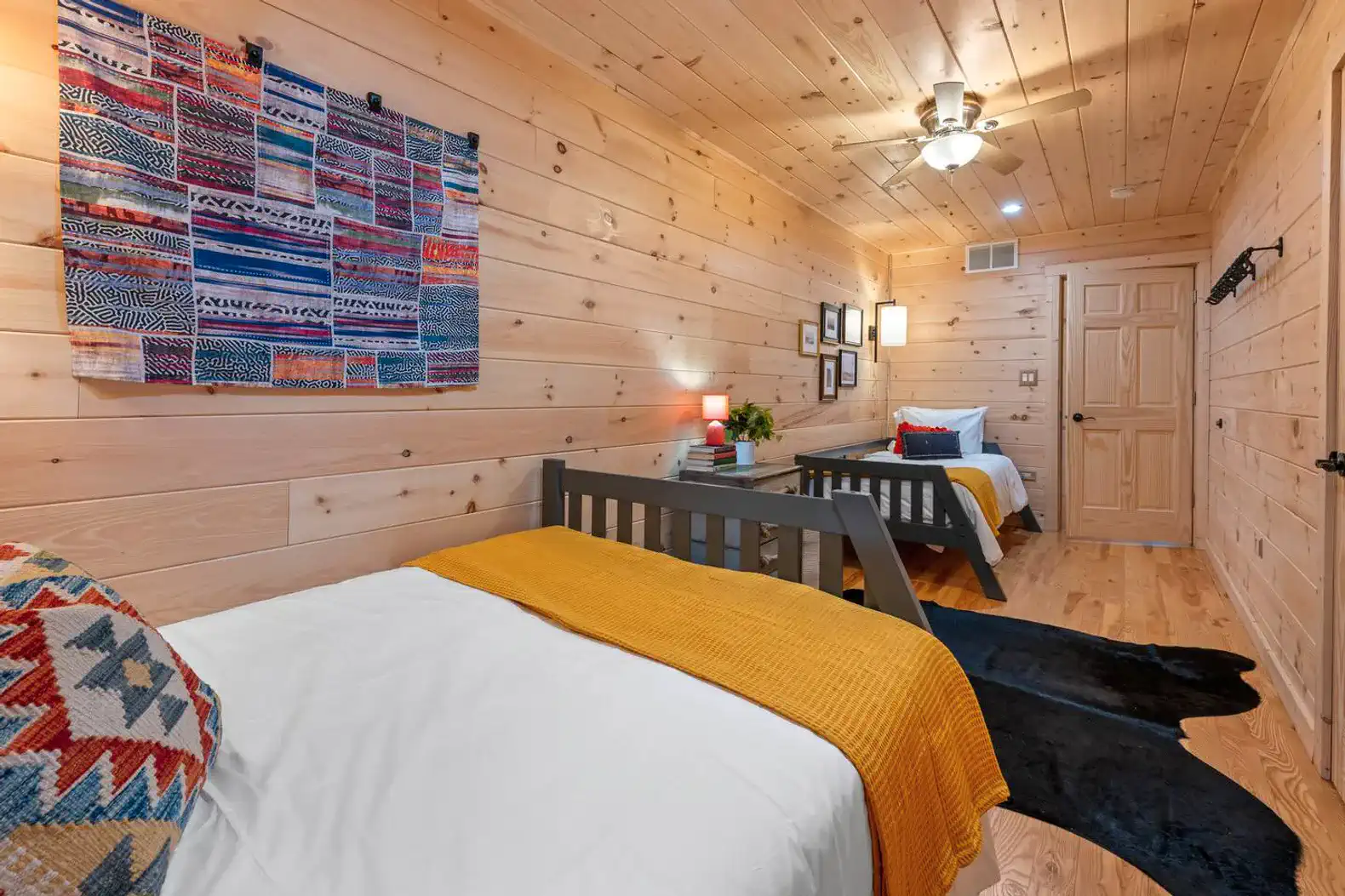 Cozy guest bedroom with two beds, wooden walls, and colorful decor