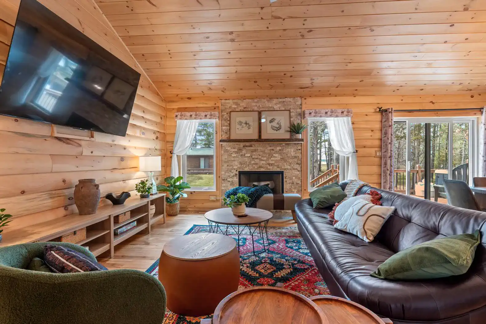 Cozy living room with wooden walls, fireplace, and large windows overlooking the outdoors