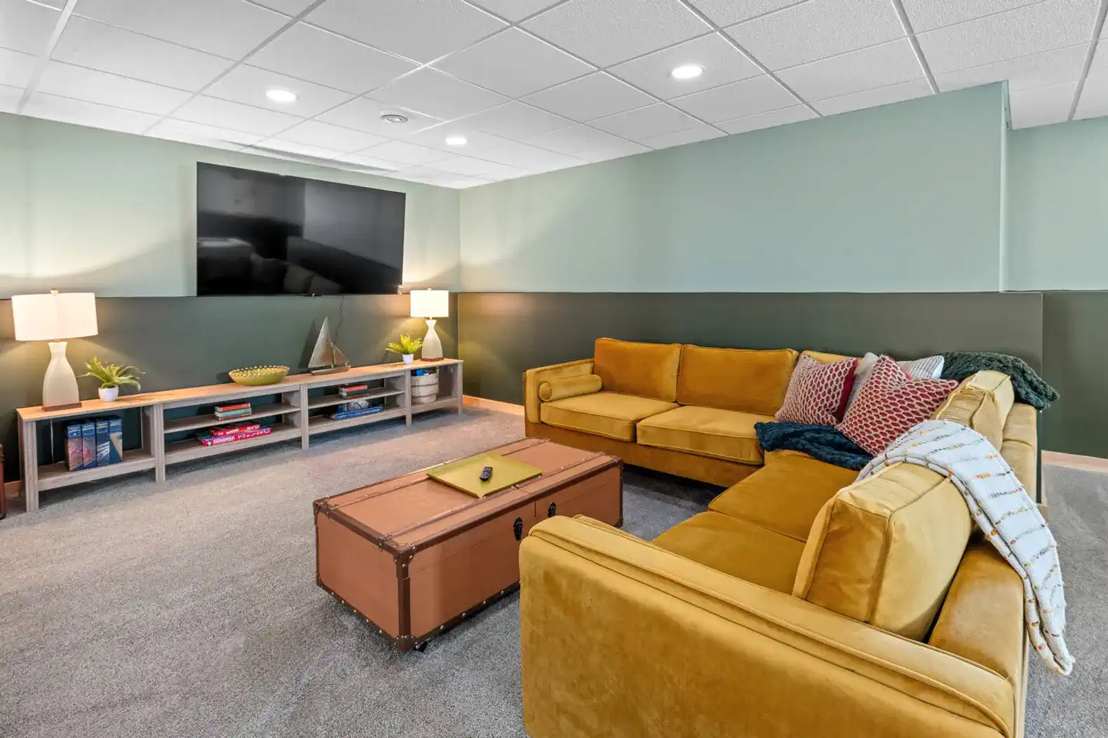 Cozy game room with yellow sofas, a coffee table, and a large TV