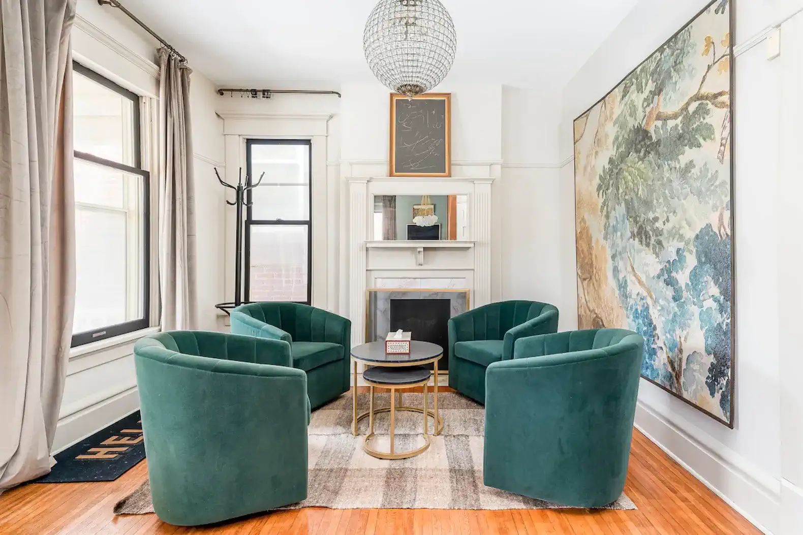 Cozy living room with green chairs, a round table, and a large artwork on the wall