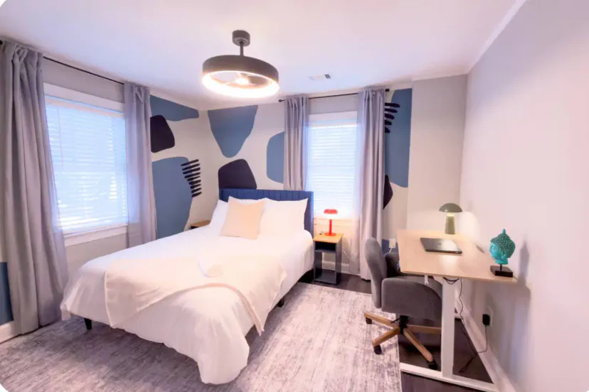 Modern bedroom thoughtfully designed with a cozy queen bed, artistic accent wall, warm lighting, and a dedicated workspace, perfect for both relaxation and remote work.