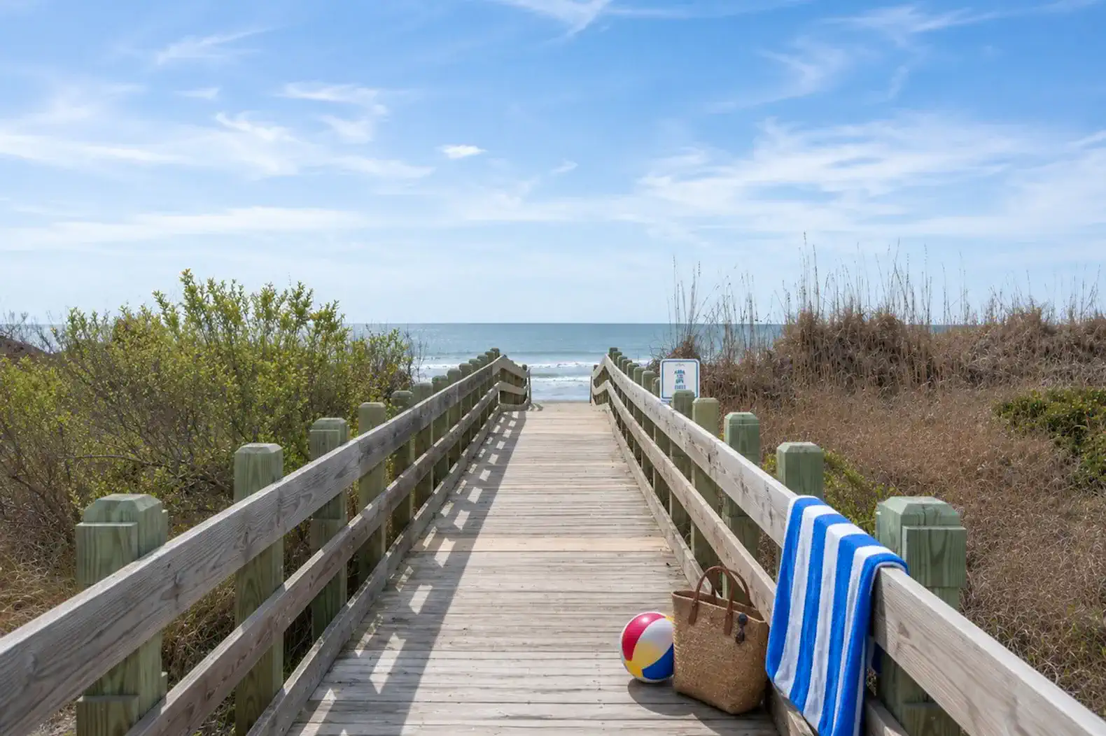 Wooden walkway leading to the beach with a beach ball and towel on the side