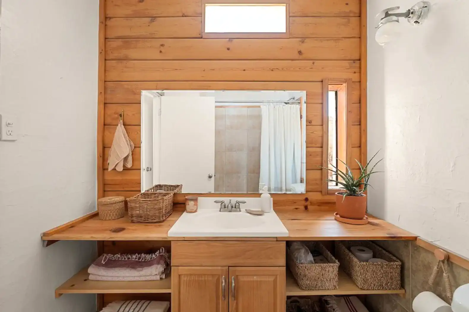 Wooden bathroom with a large mirror, sink, and natural light from a window