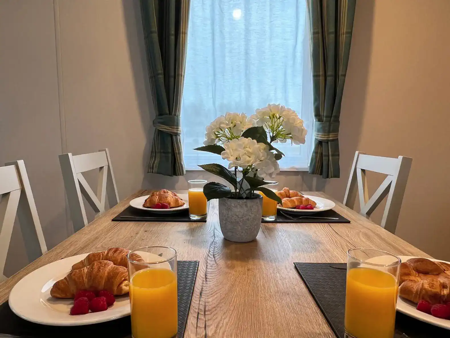 Dining table set with croissants, raspberries, and orange juice in a cozy setting