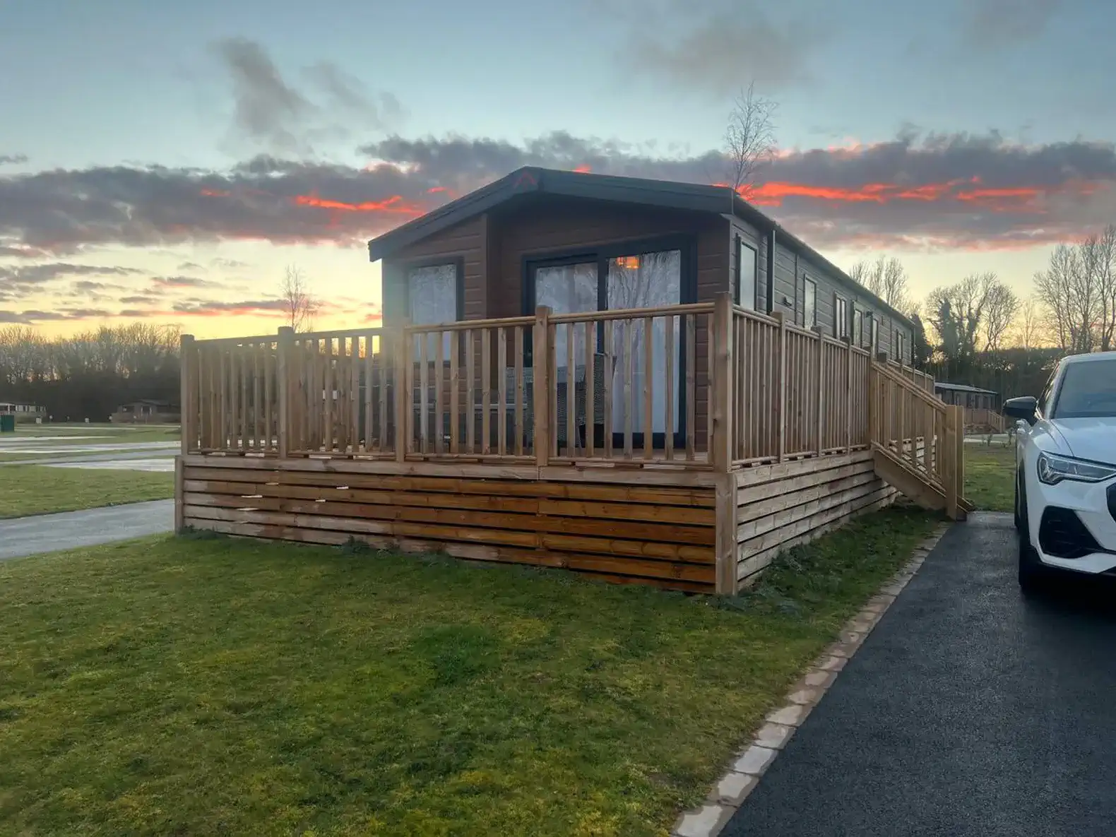 Exterior view of a wooden cabin with a deck and sunset sky