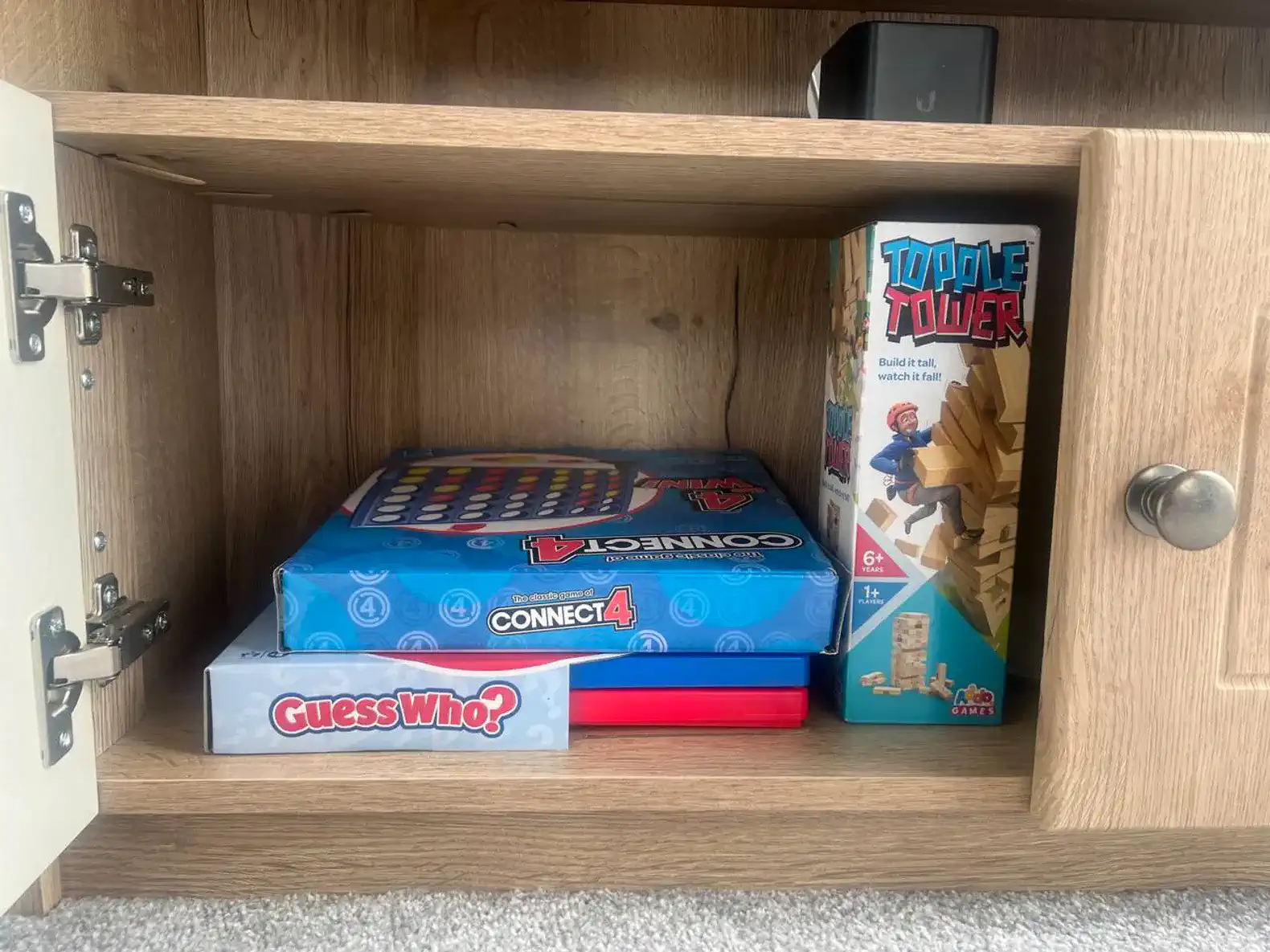 Games stored in a wooden cabinet including Connect 4 and Guess Who