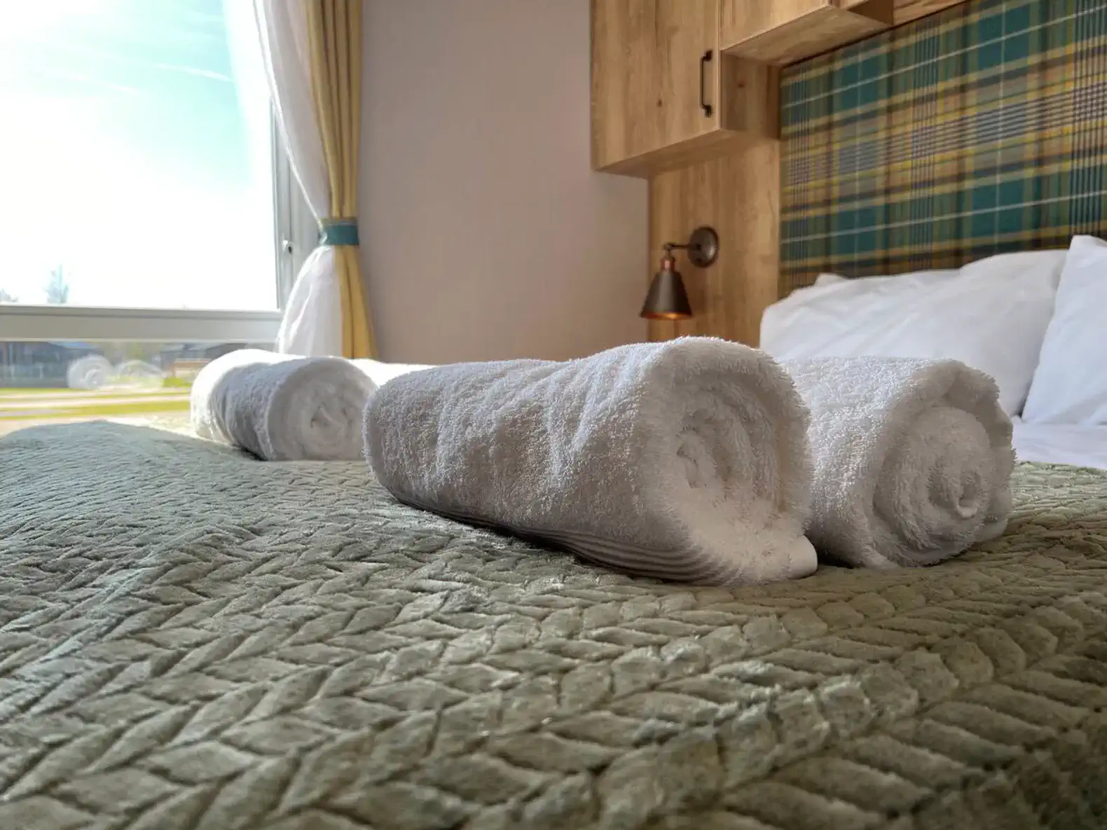 Rolled towels neatly arranged on a bed with a green cover and plaid headboard