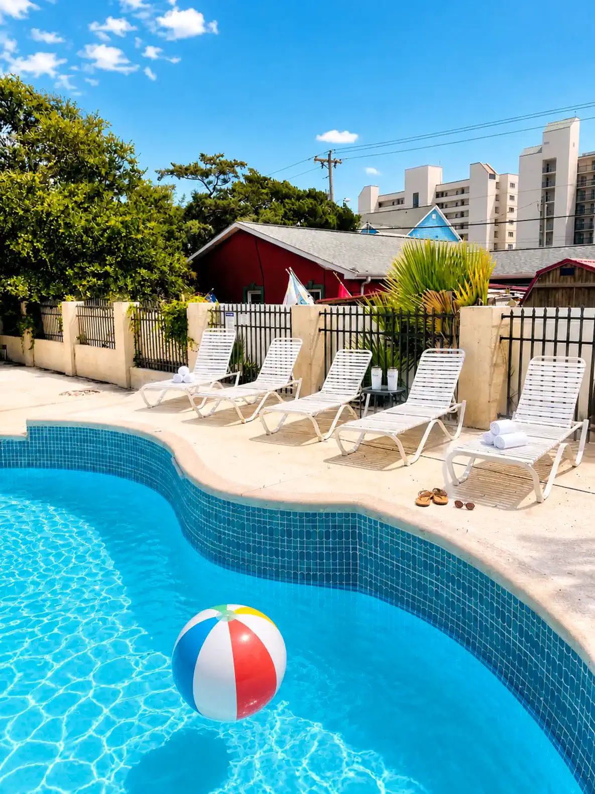 Inviting pool area with lounge chairs and a beach ball under a clear blue sky