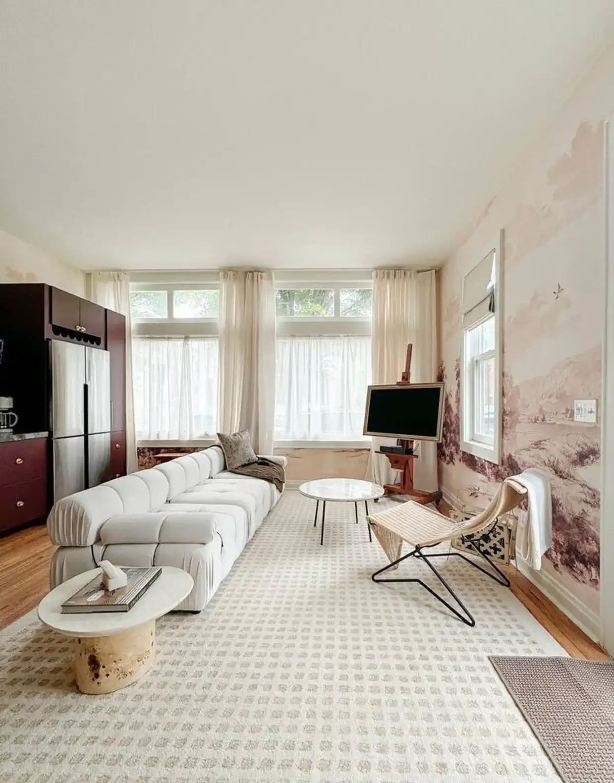 The bright living room comes with a full sized couch, lounge chair, and frame TV. It sits in front of the studio kitchen, and has two layers of curtains to allow light to filter in, while providing privacy from the street.