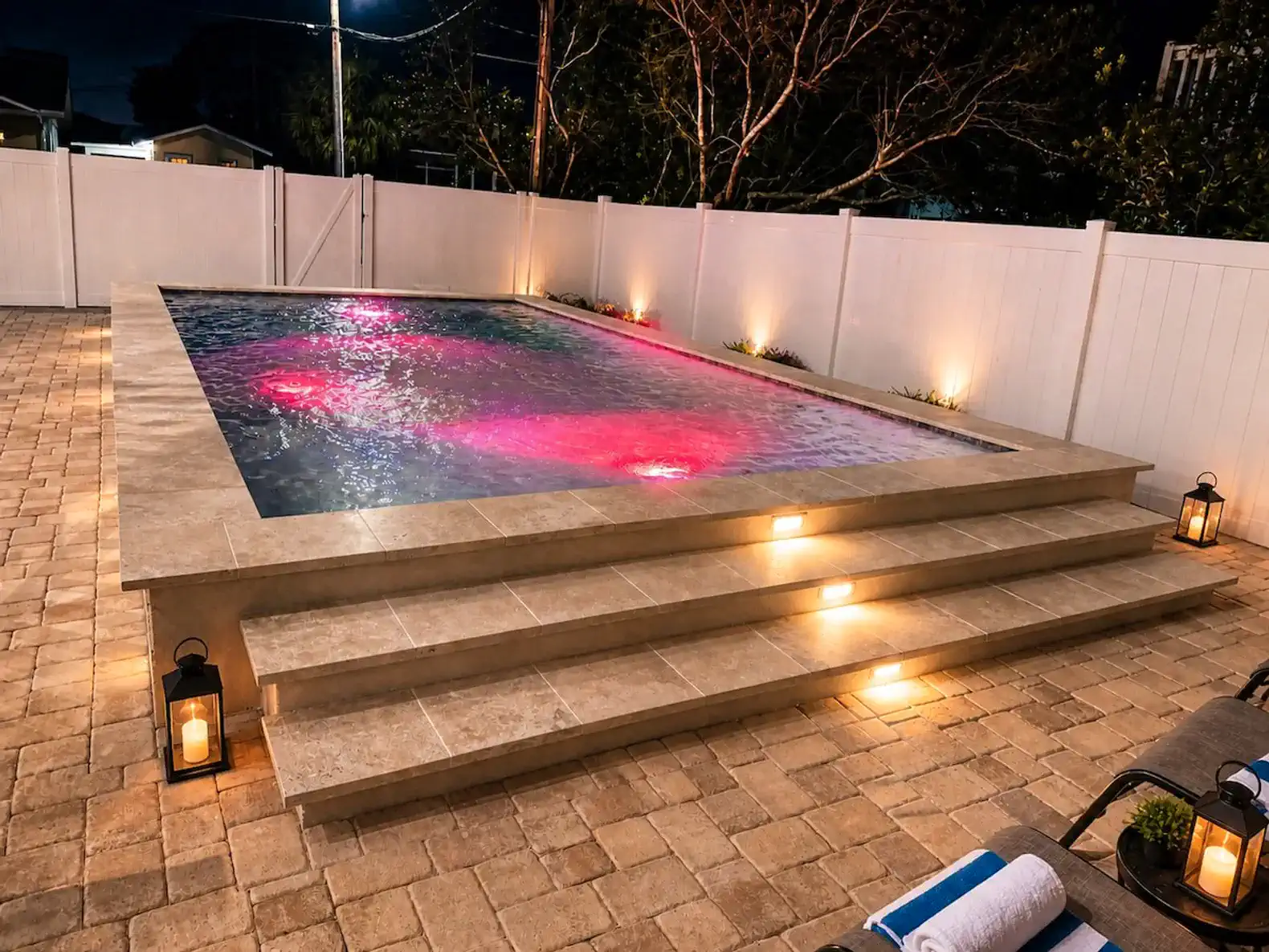 Illuminated pool with steps and surrounding patio area at night