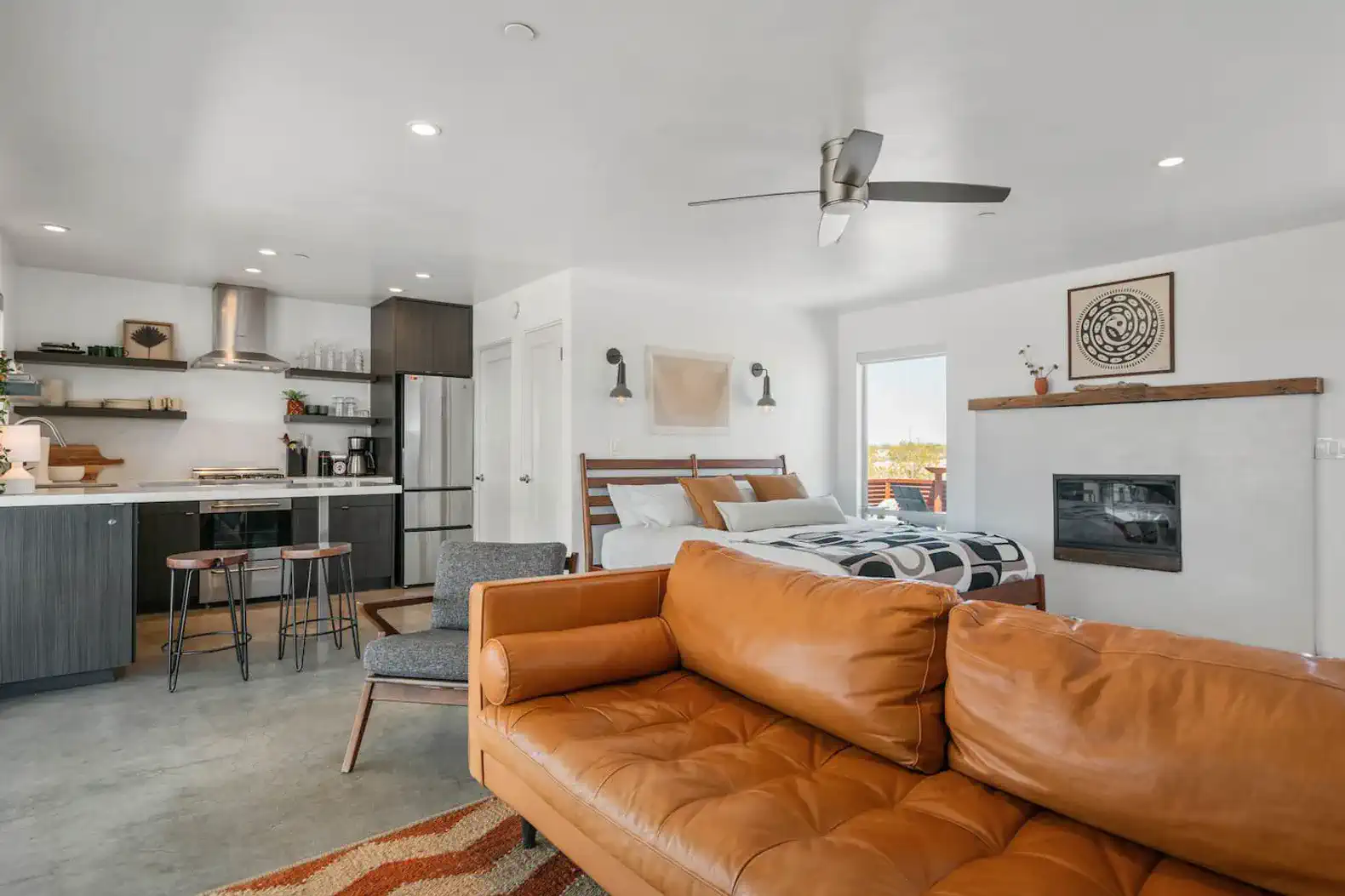 Stylish living area with a leather sofa, kitchenette, and a cozy bed in the background