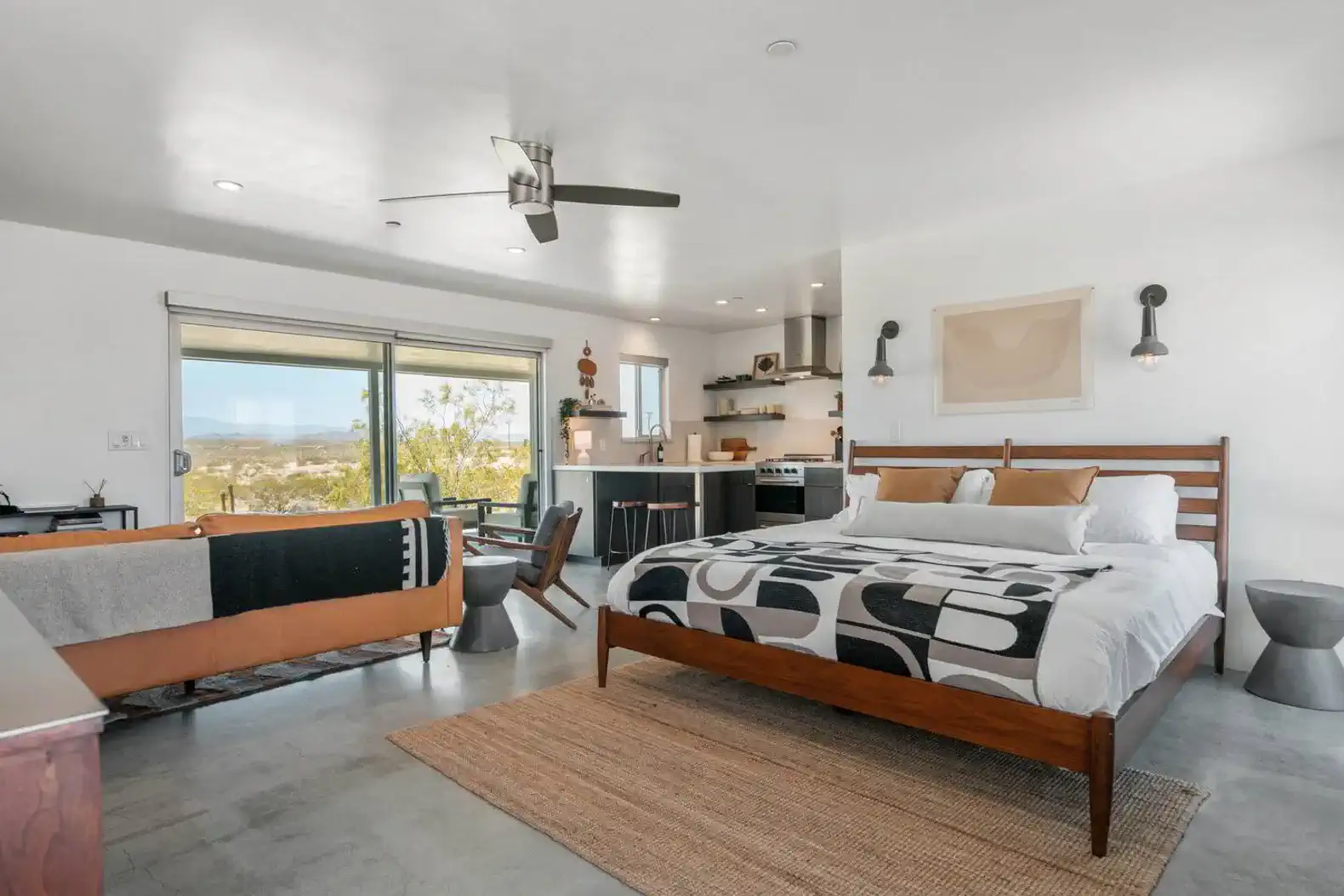 Spacious master bedroom with a king bed, kitchenette, and large windows showcasing desert views