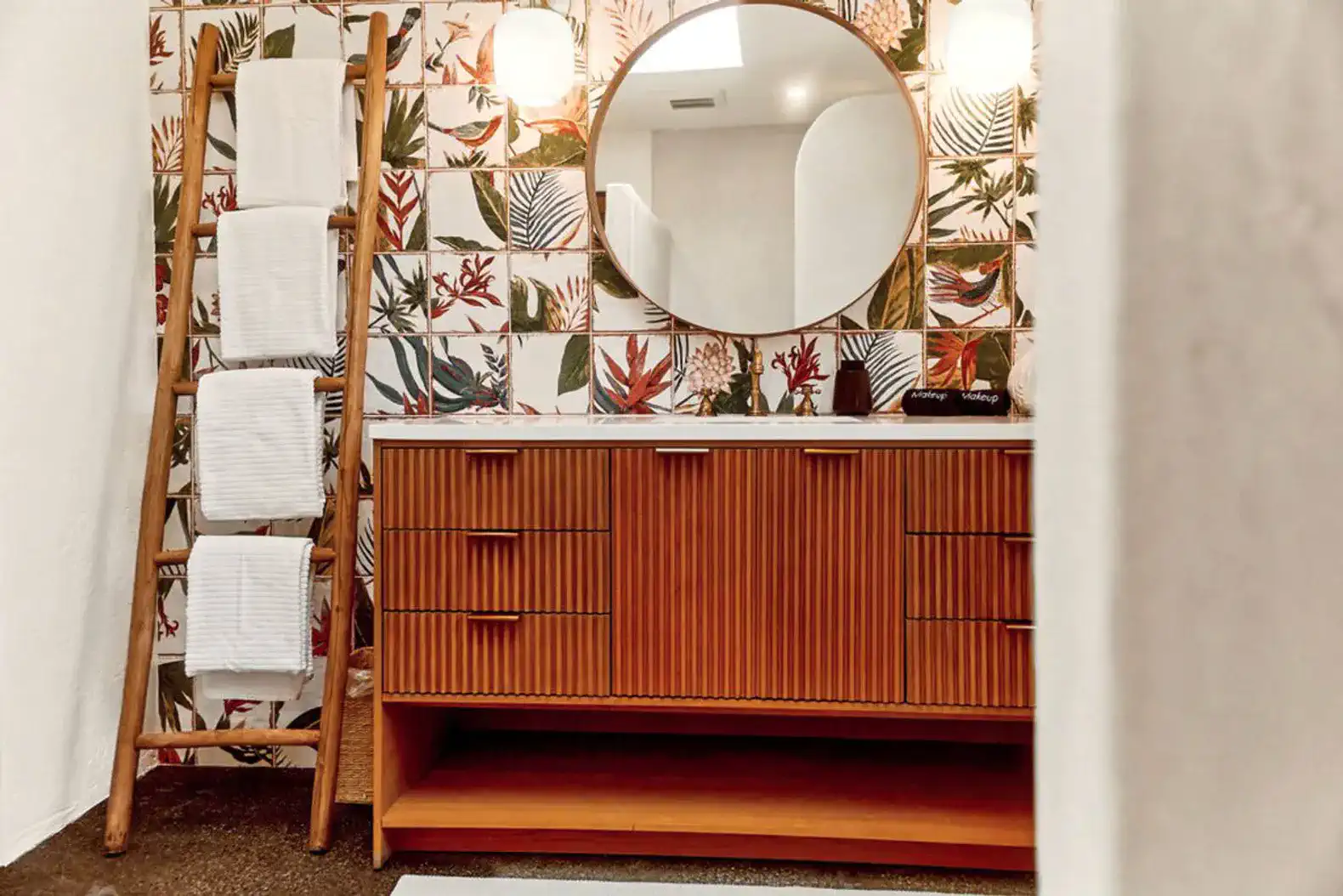 Stylish bathroom with wooden vanity, round mirror, and tropical patterned wall tiles