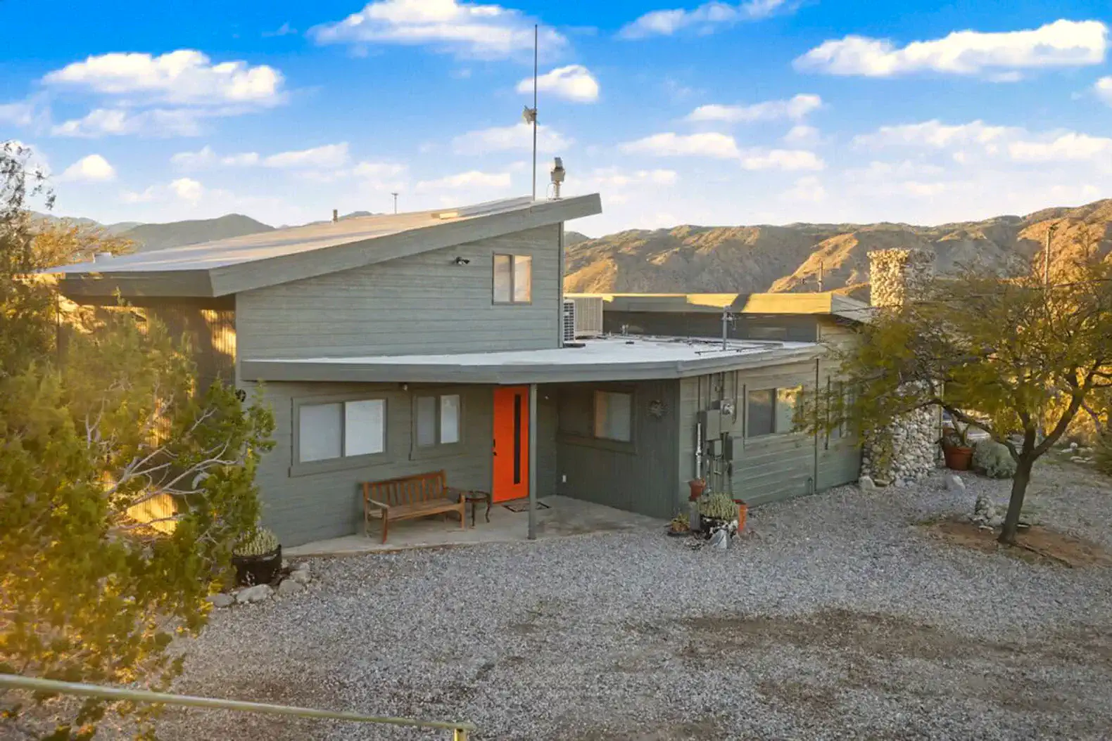 Hilltop desert home with orange door and gravel driveway surrounded by mountains