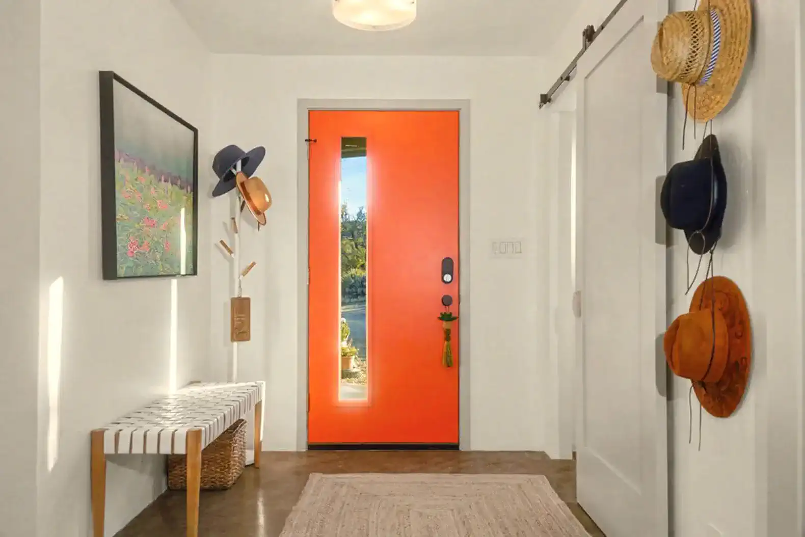 Bright orange front door with hats hanging on the wall and a stylish bench