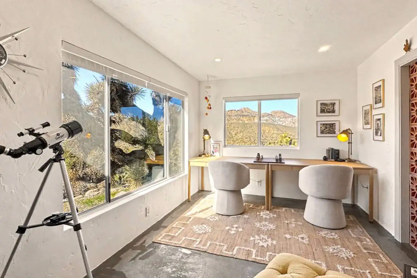 Bright workspace with two chairs, large window showcasing desert views and a telescope