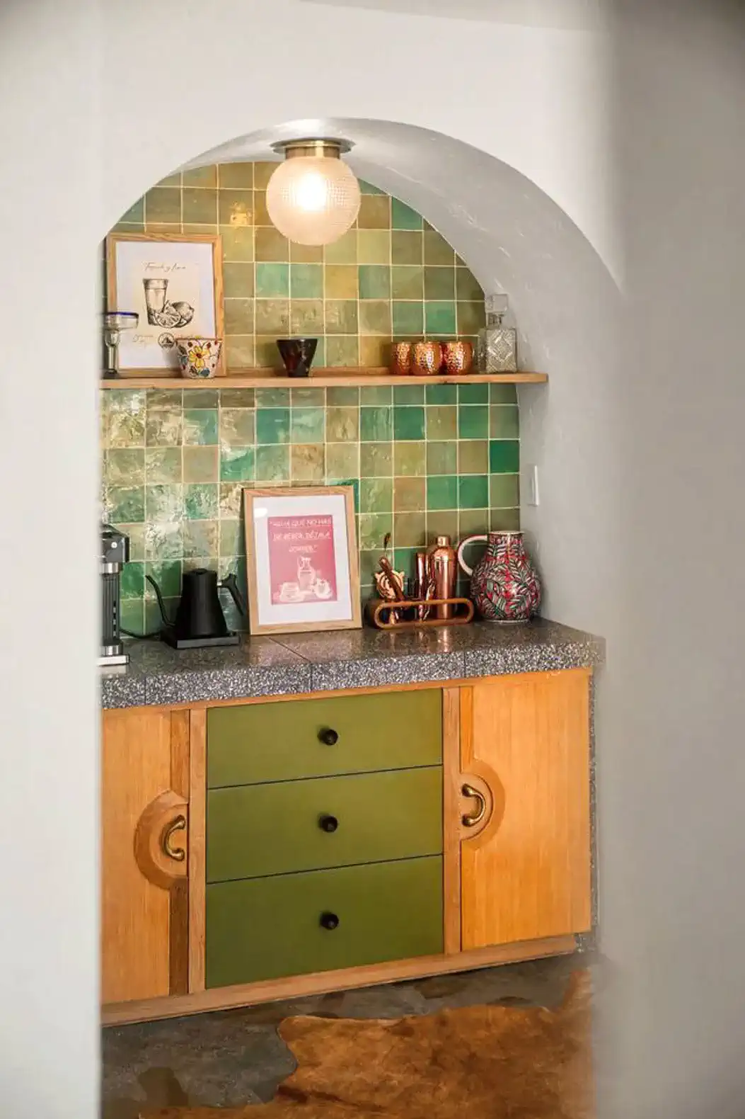 Stylish kitchen with green and wooden cabinetry, colorful tile backsplash, and decorative items