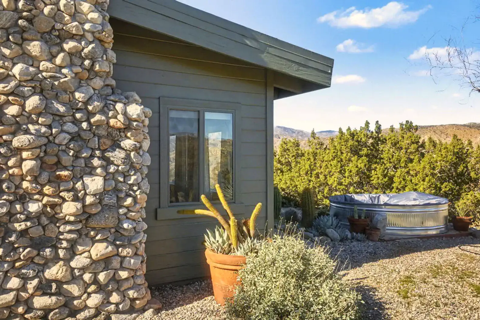Exterior view showcasing stone wall, potted plants, and hot tub surrounded by desert landscape