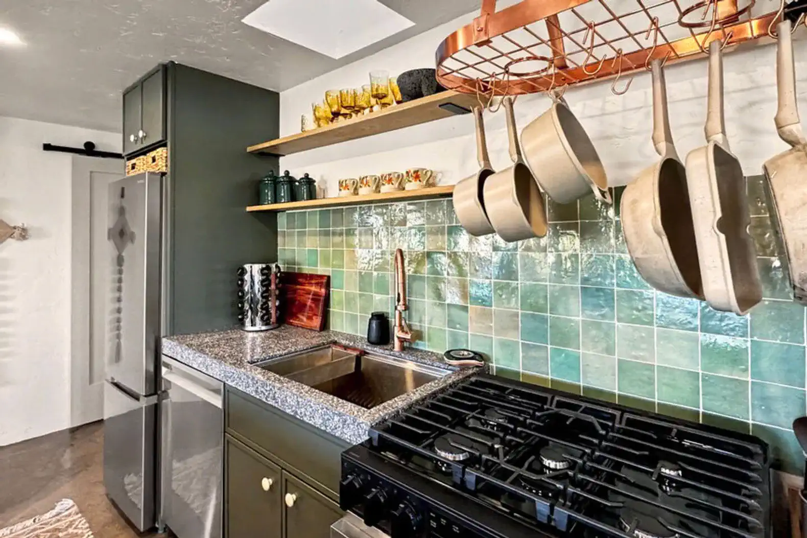 Modern kitchen with green tiles, hanging pots, and sleek appliances