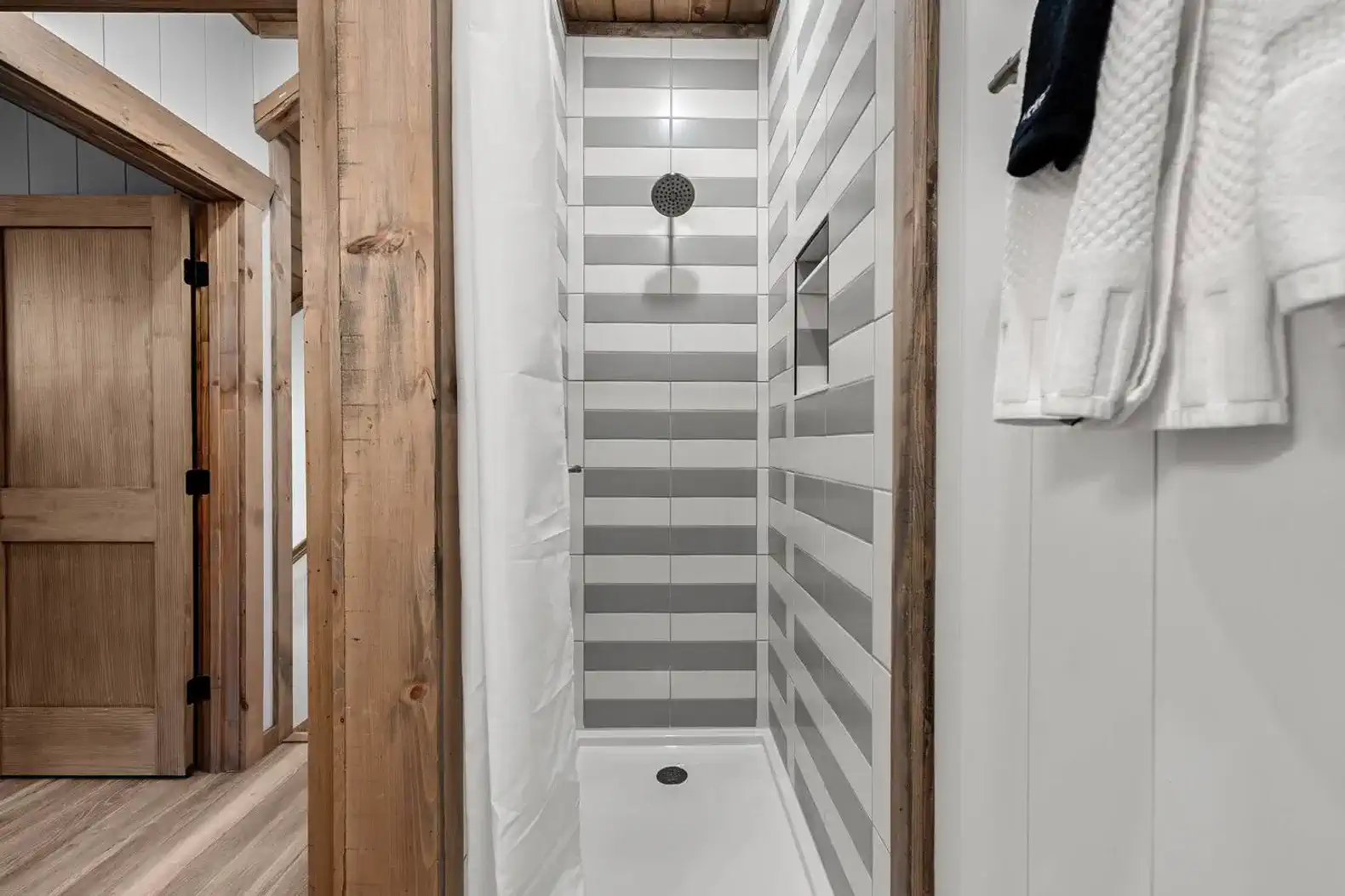 Modern shower with striped tile design and wooden accents