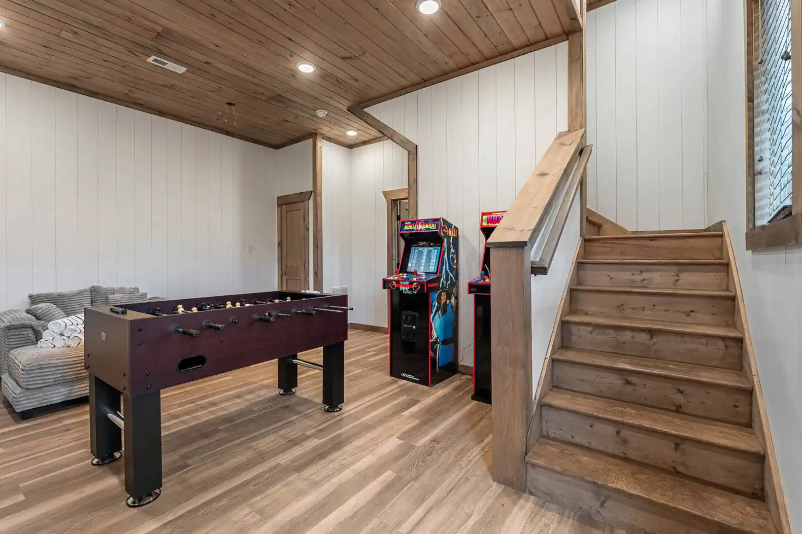 Game room featuring foosball table and arcade machines with wooden stairs