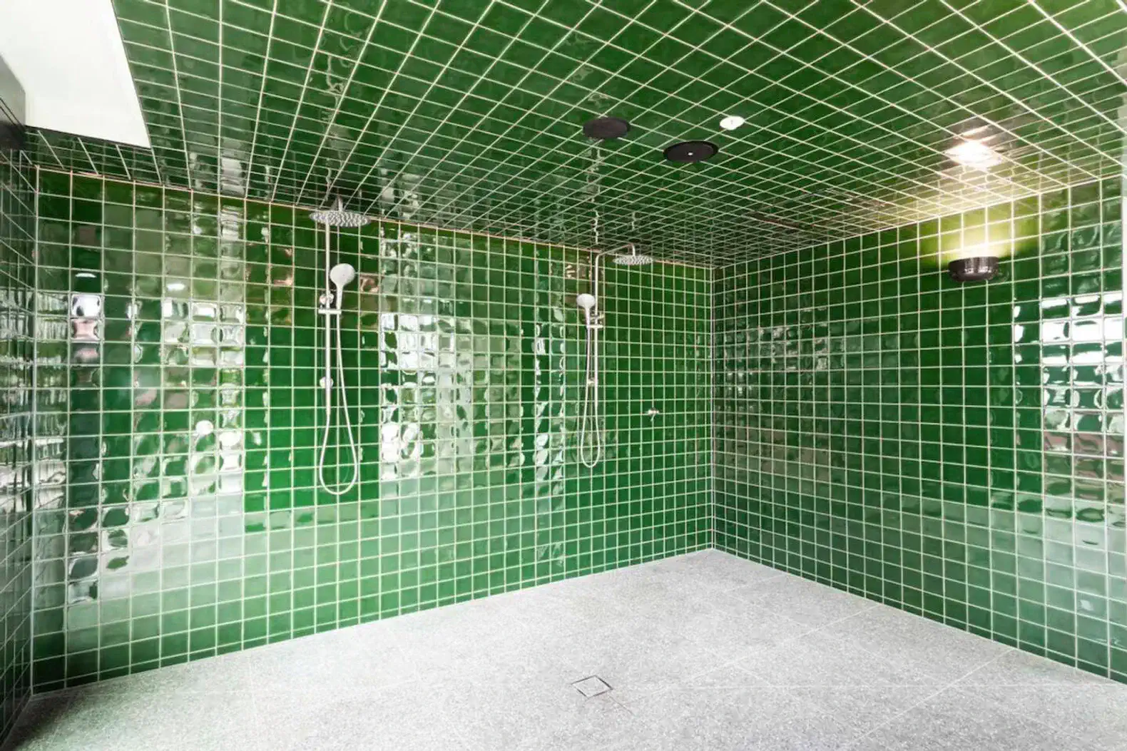 Spacious bathroom with green tiled walls and multiple showerheads