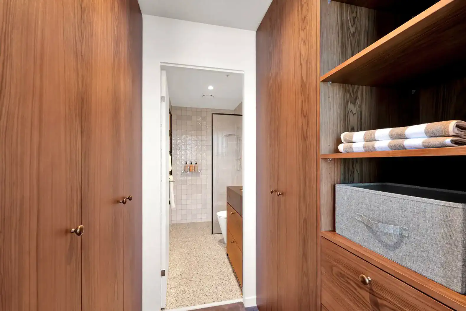 Wooden cabinetry leading to a modern bathroom with tiled walls