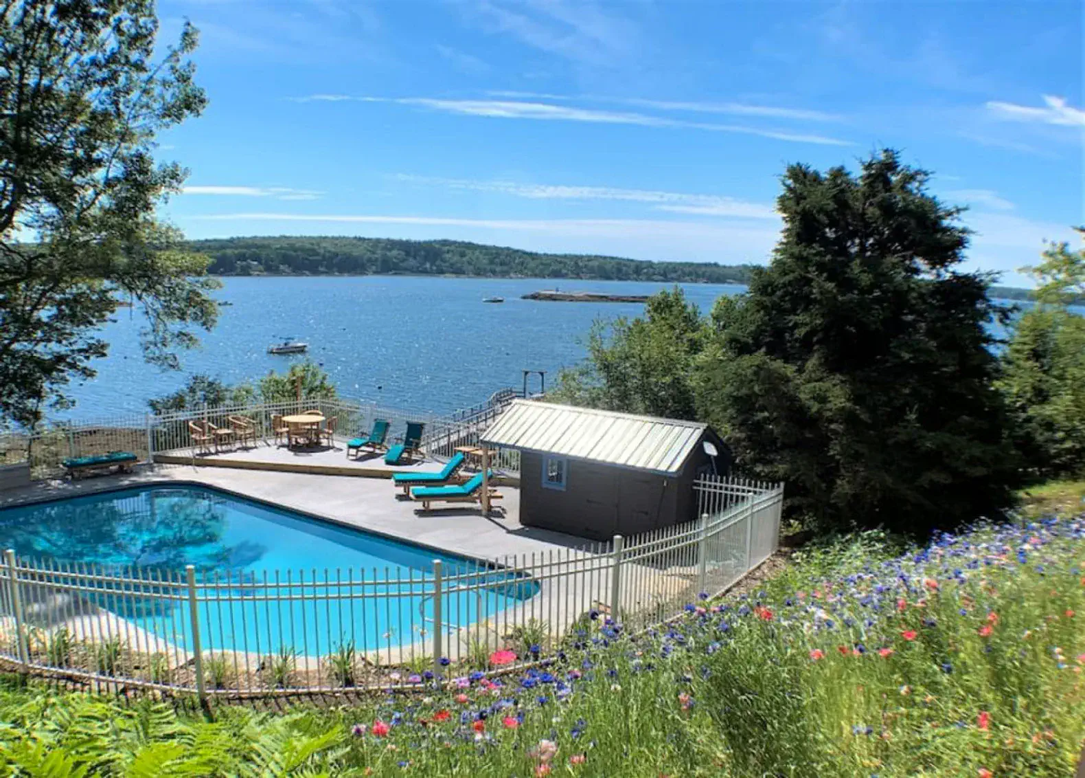 Vista escénica de un área de piscina con vista al agua, con tumbonas y flores vibrantes