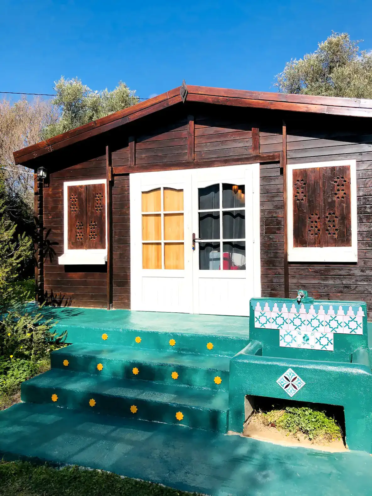 Charming wooden cabin entrance with decorative shutters and colorful steps
