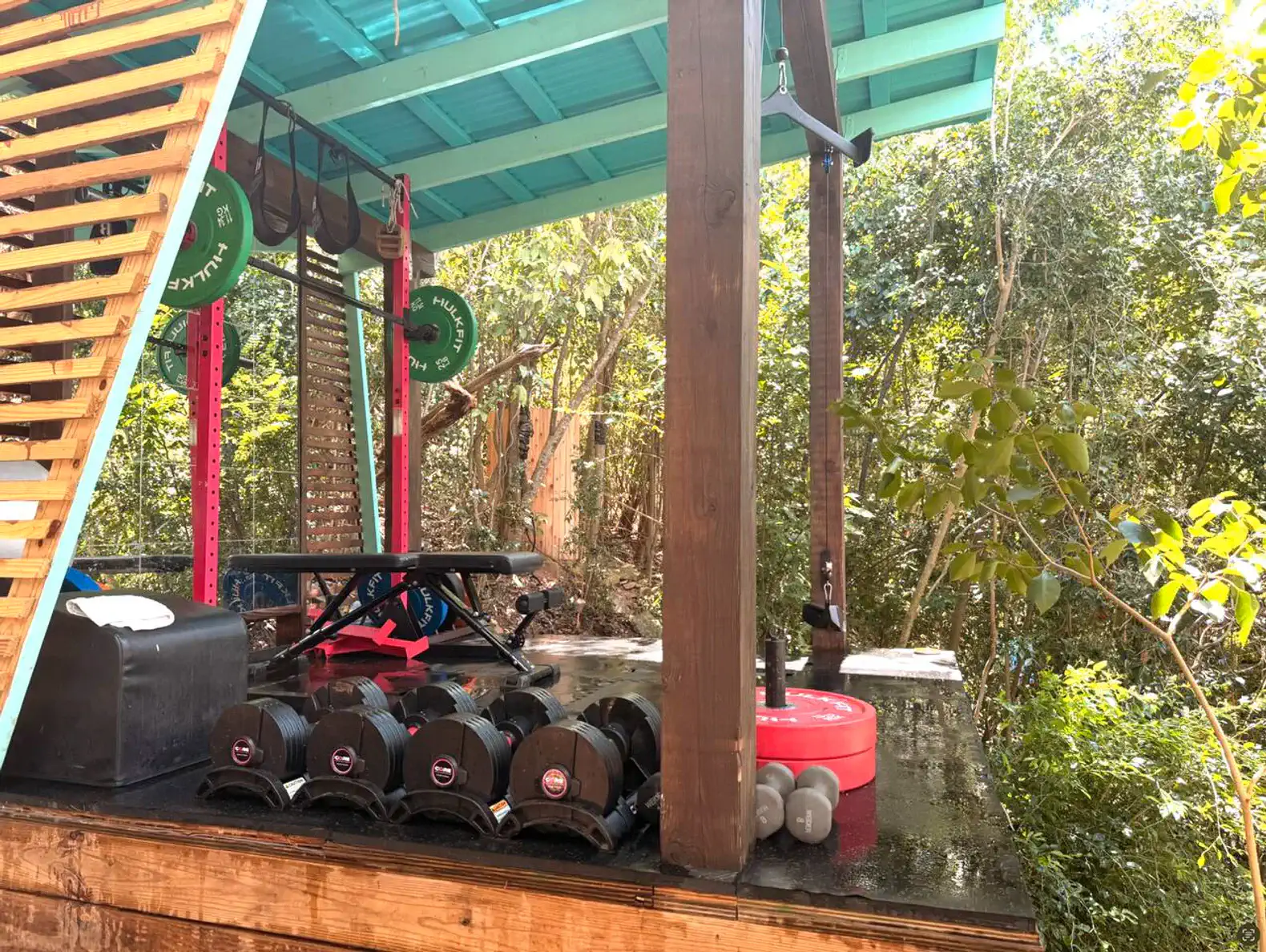 Outdoor gym area with weights and exercise equipment surrounded by greenery