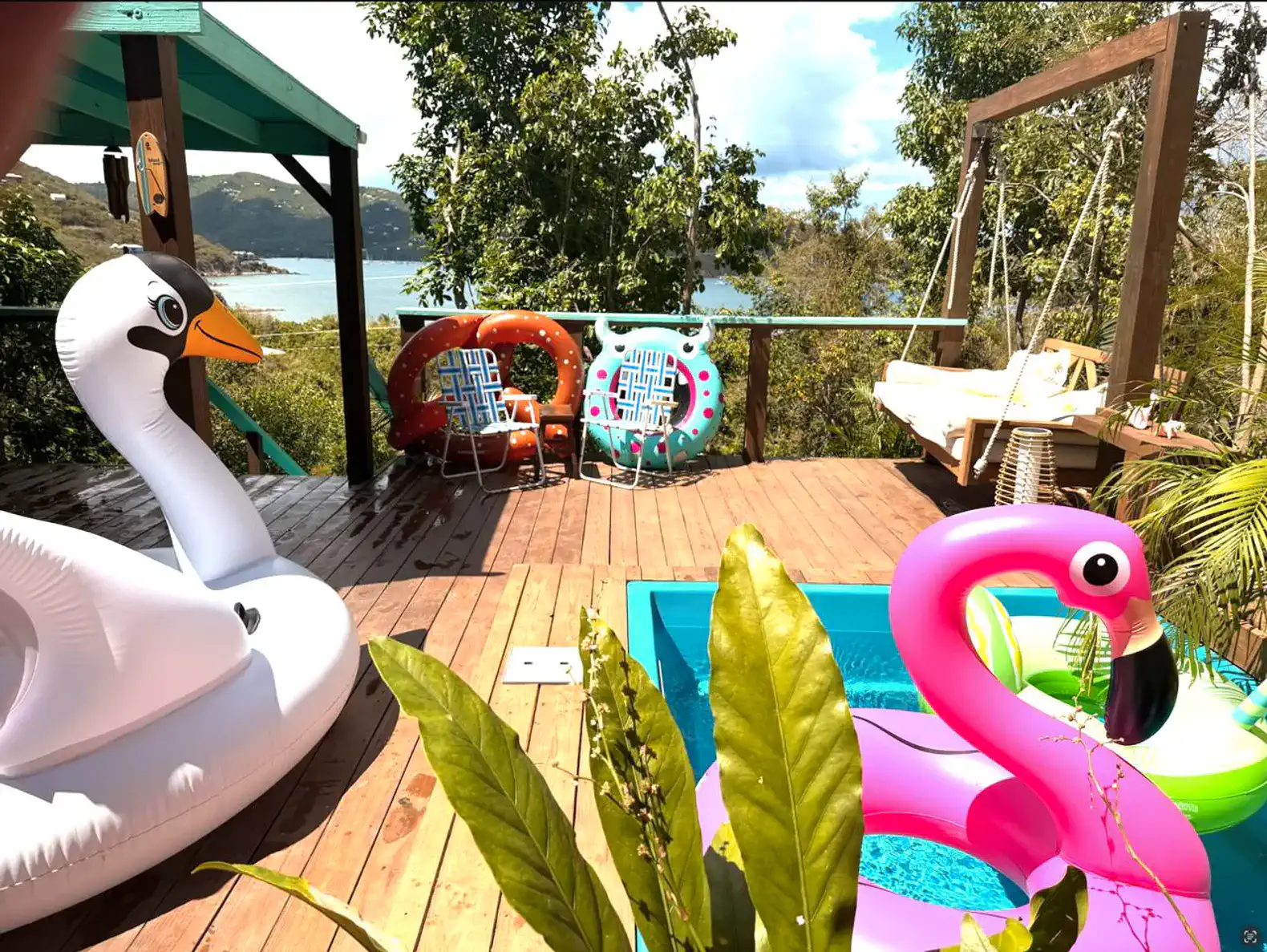 Colorful pool floats beside a small pool on a wooden deck with a scenic view