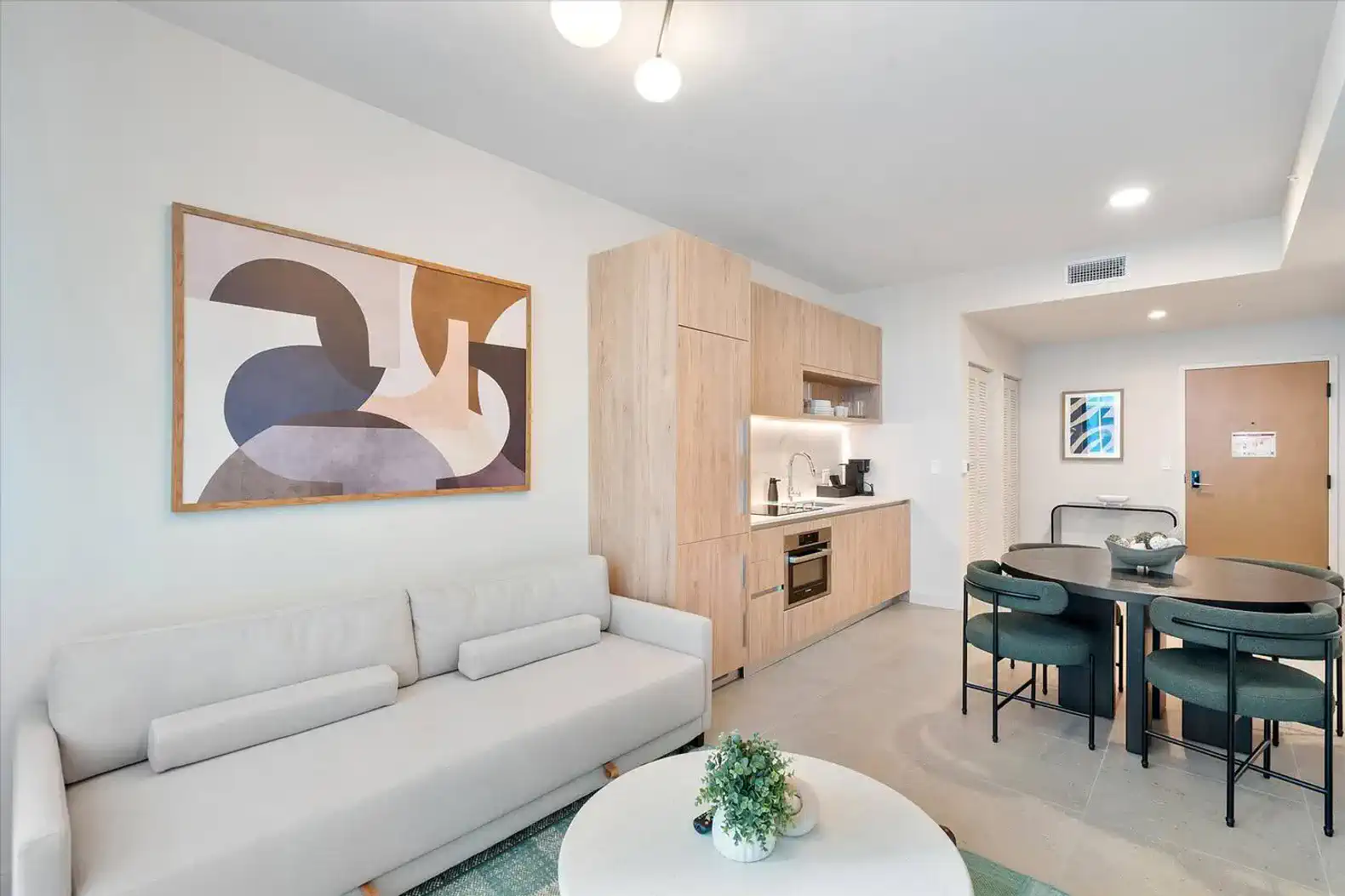 Modern living area with a sofa, dining table, and kitchenette featuring wood cabinetry