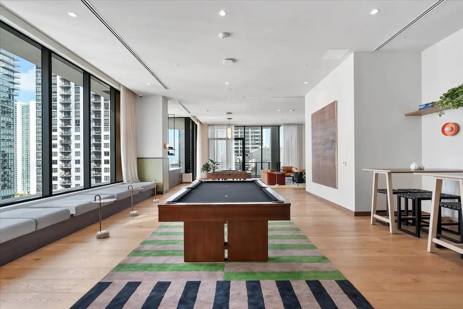 Spacious game room with a pool table and large windows offering city views