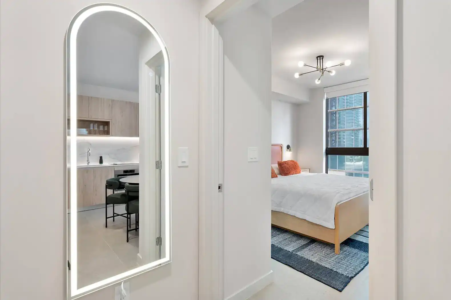 Modern hallway with a mirror leading to a bedroom and kitchen area