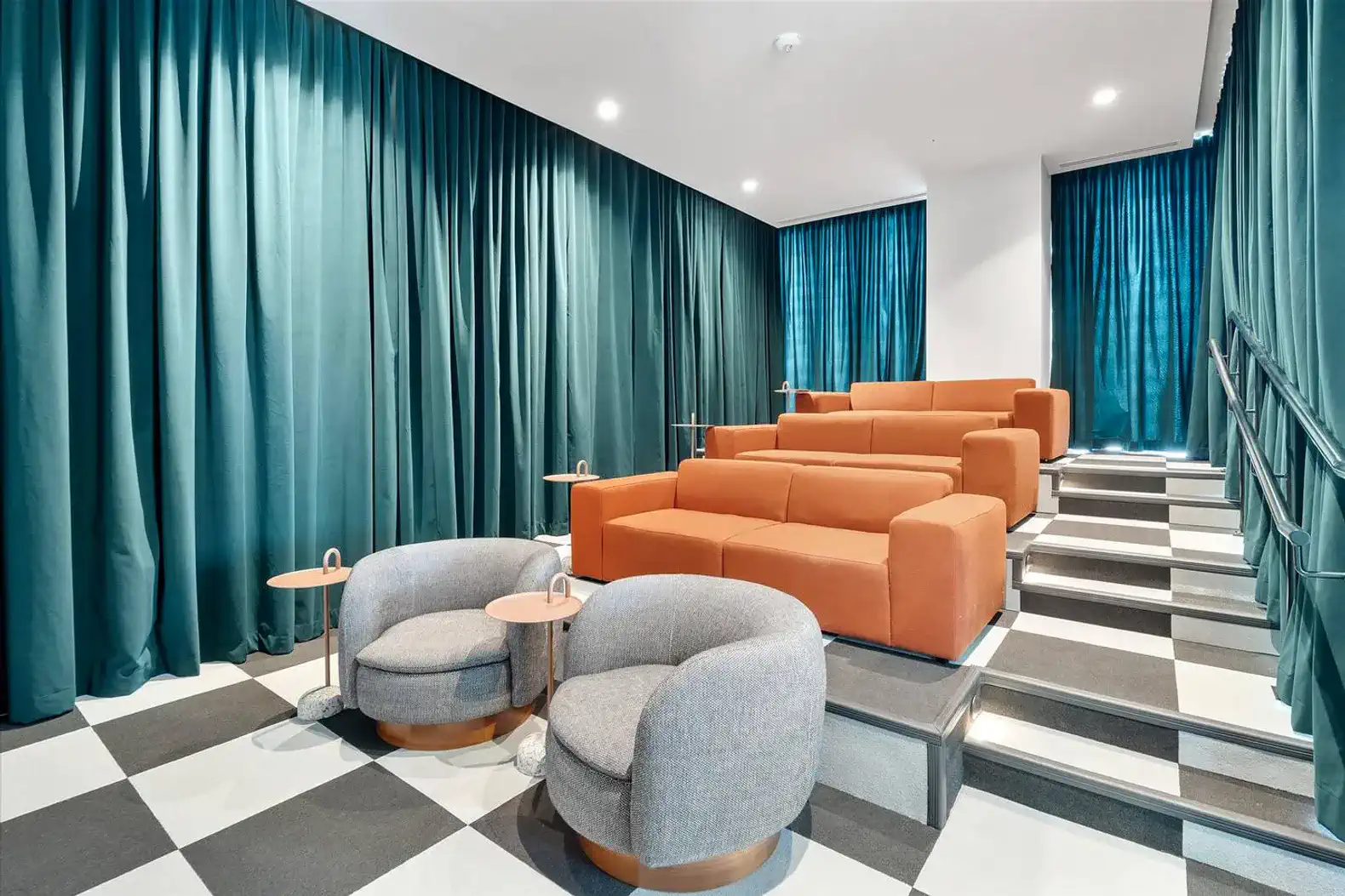 Stylish lounge area with orange sofas and gray chairs against teal curtains