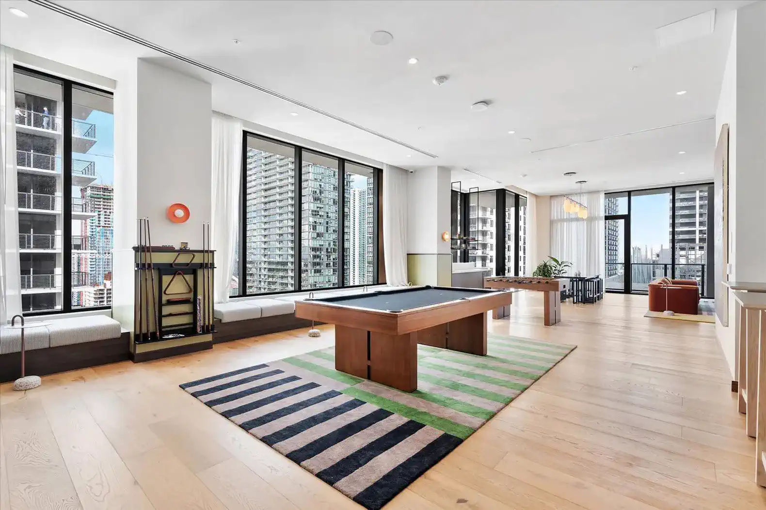 Spacious game room with a pool table and large windows offering city views