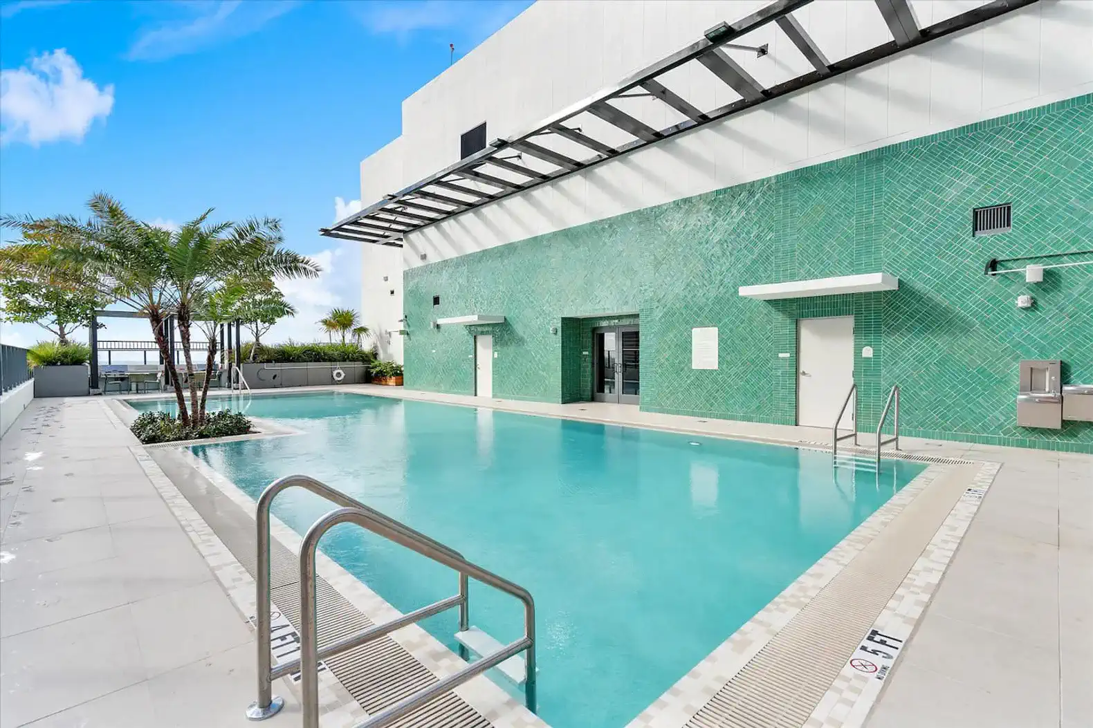 Spacious outdoor pool surrounded by green tiles and palm trees