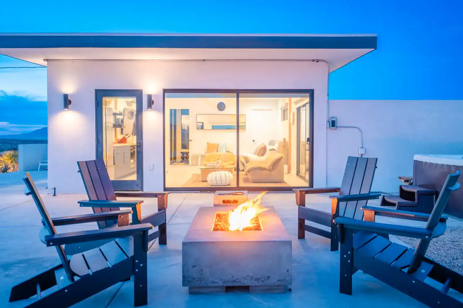 Outdoor firepit surrounded by chairs with a view of the modern living area through large glass doors