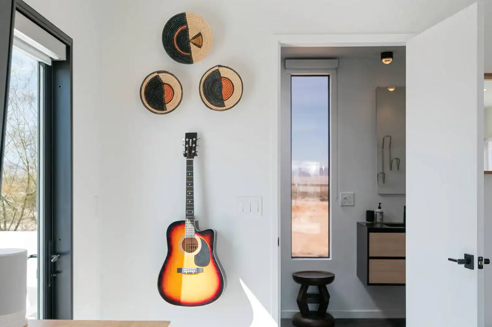 Decorative wall with woven baskets and a guitar near a modern bathroom entrance