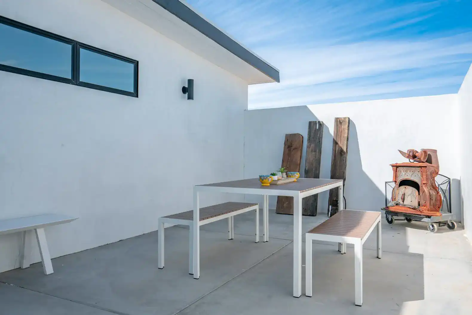 Outdoor dining area with a table and benches against a white wall