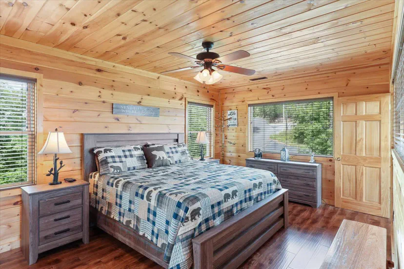 Cozy master bedroom with wooden walls, a king-size bed, and large windows letting in natural light