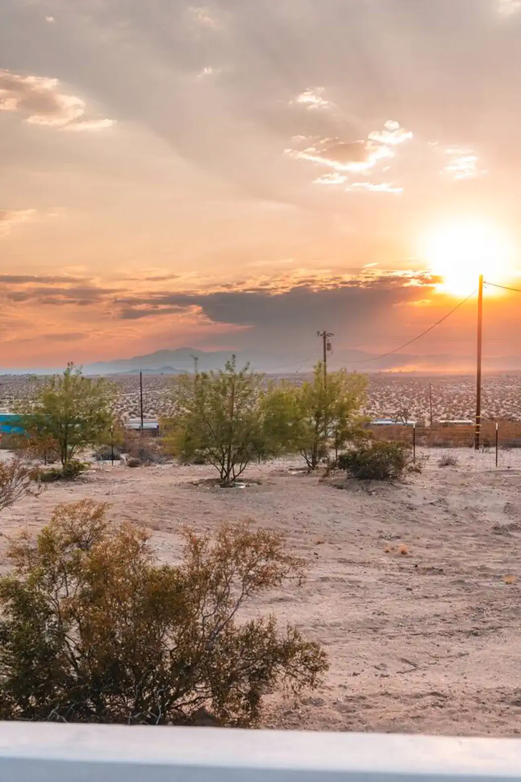 Desert landscape at sunset with distant mountains and sparse vegetation