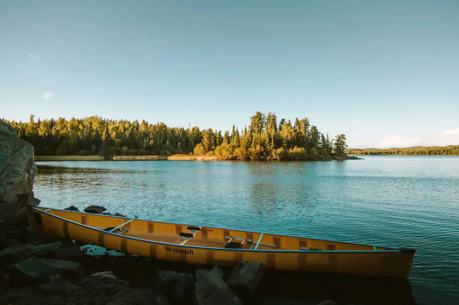 Canoe resting on rocky shore with serene lake and forested island in the background
