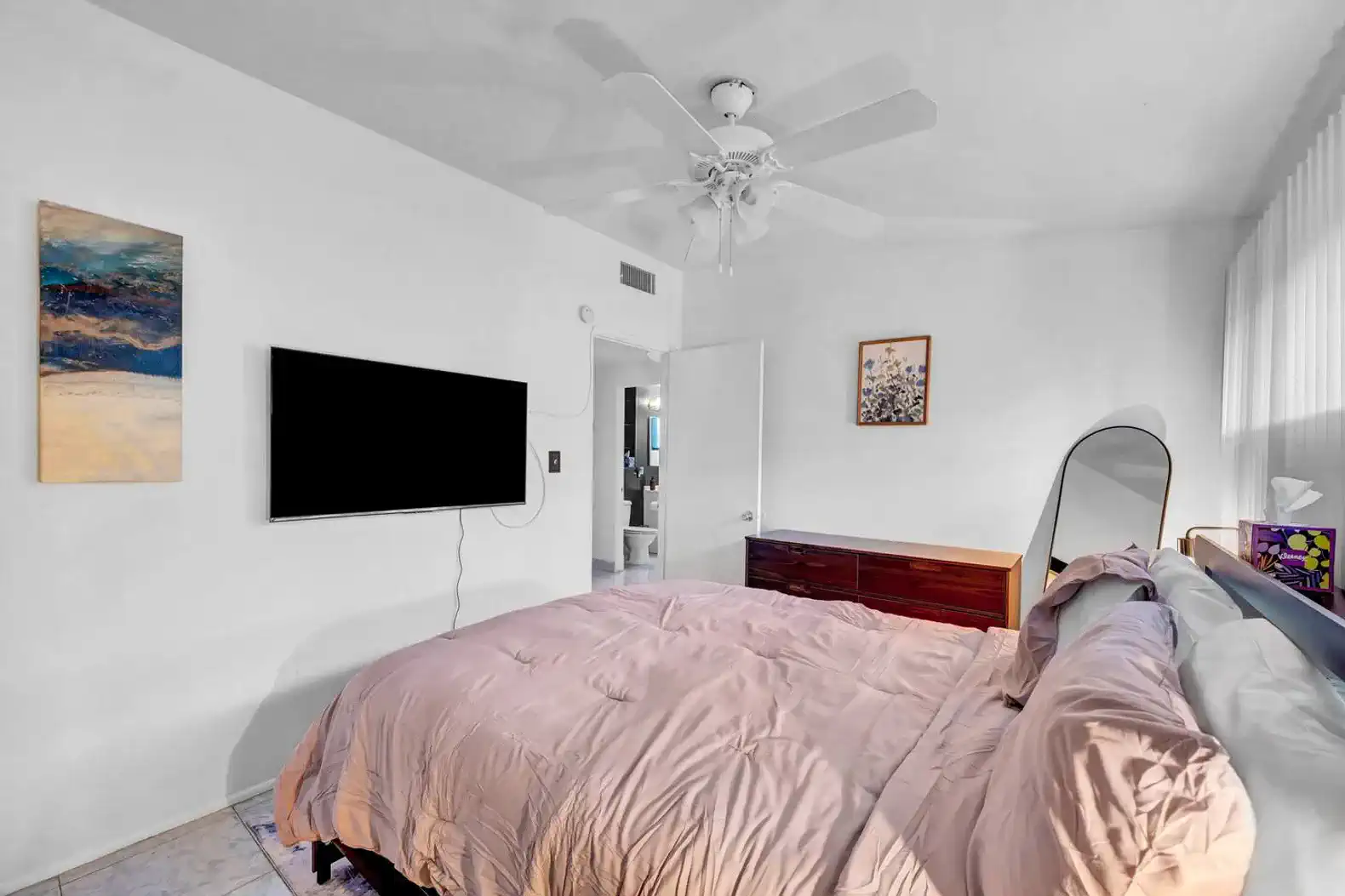 Cozy master bedroom with a pink comforter, TV, and access to an en-suite bathroom